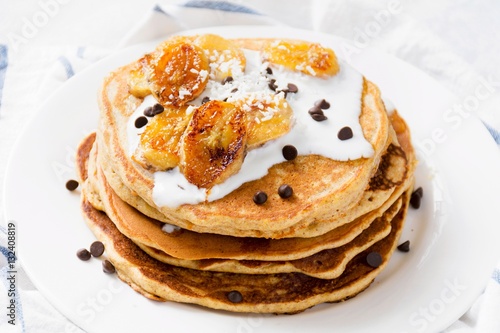 Banana pancakes with yogurt and chocolate chips on white plate, close up view