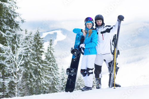 Happy couple standing on a mountain top. Couple skiing and snowboarding outside in the mountains.