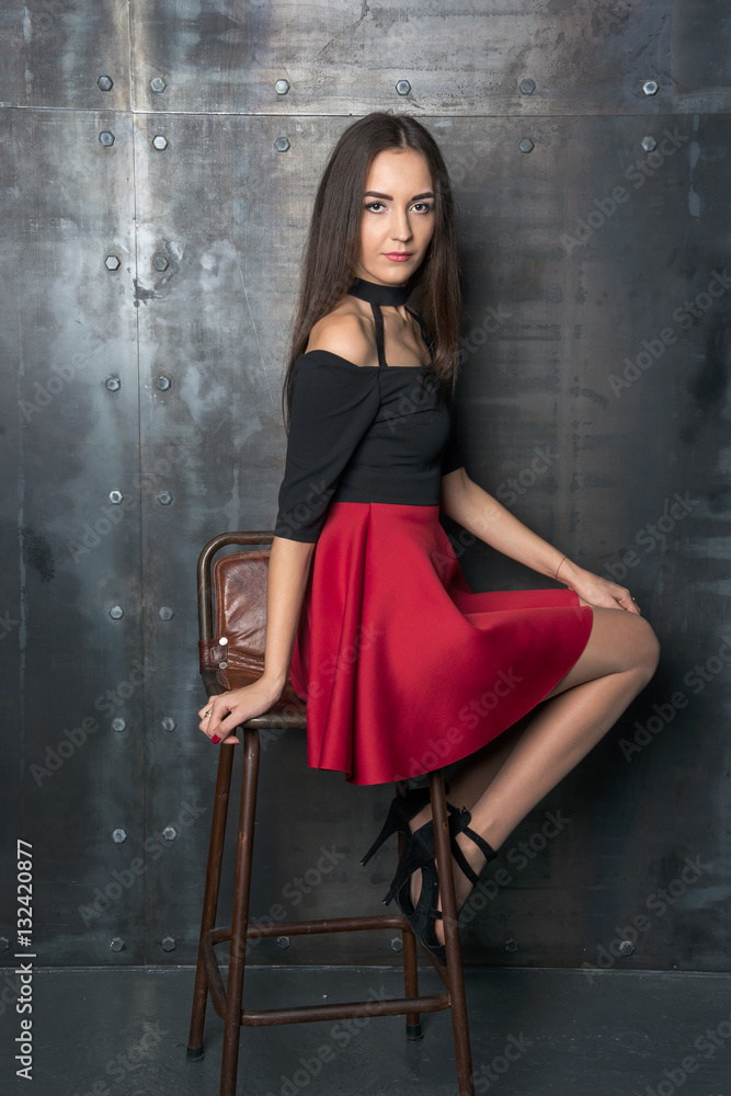 Beautiful woman in a short dress sits on a chair beside the wall foto ...