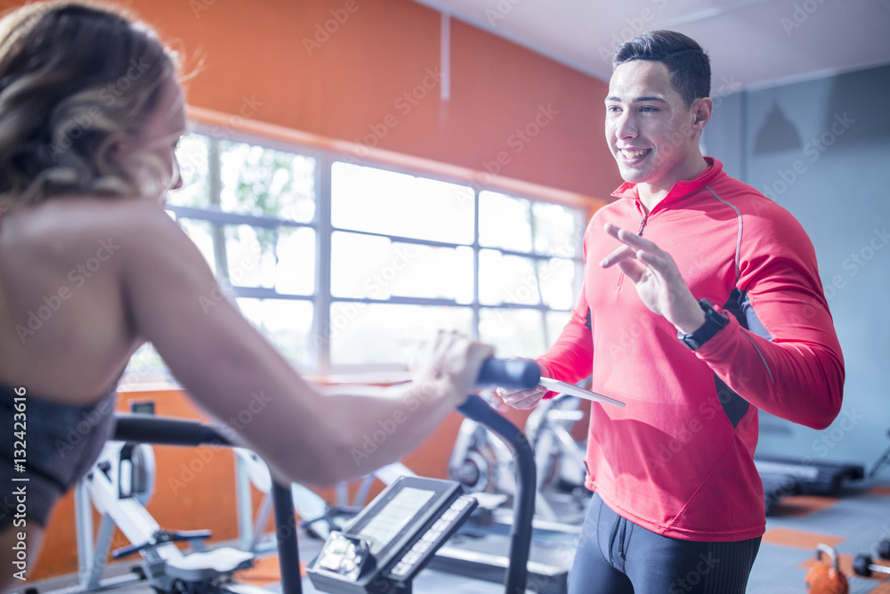 Fitness instructor talking to woman on exercise machine Fitness instructor talking to woman on exercise machine
