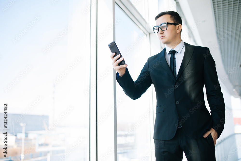 Handsome businessman in suit use mobile phone to check email or write message in office room Handsome businessman in suit use mobile phone to check email or write message in office room