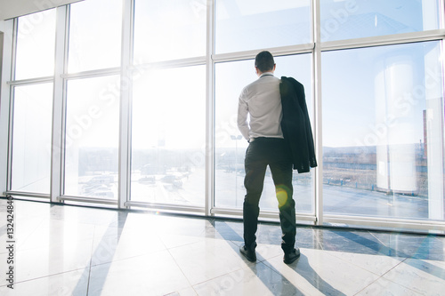 Young relaxed businessman with jacket over shoulders in modern office panoramic windows