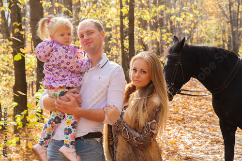 young family walking in the autumn forest with a horse
