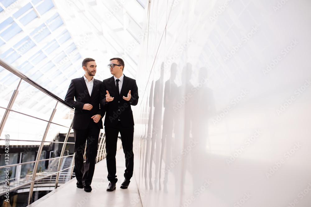 Two businessmen walking along in modern office building Two businessmen walking along in modern office building