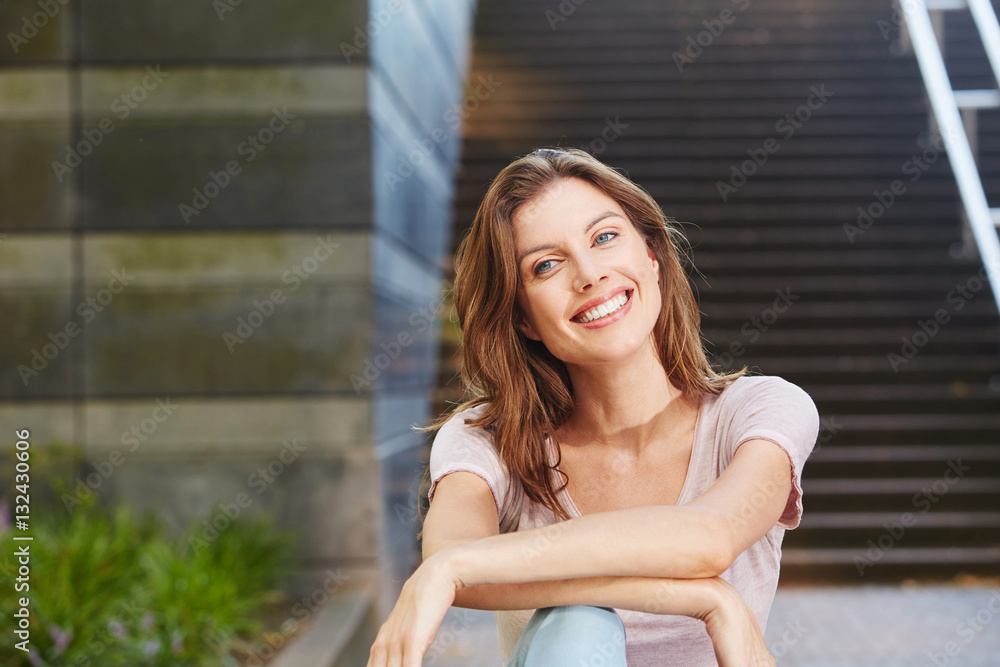 cheerful young woman sitting outdoors and smiling