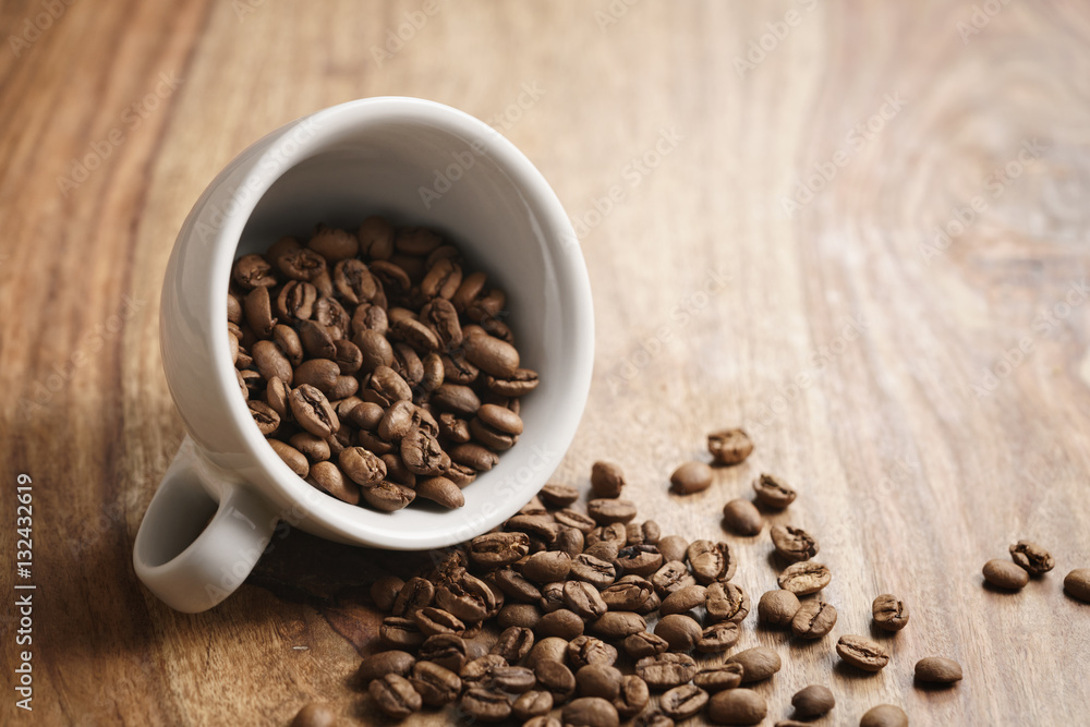overturned cappuccino cup with roasted coffee beans on wood table, with copy space overturned cappuccino cup with roasted coffee beans on wood table, with copy space