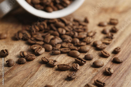 overturned cappuccino cup with roasted coffee beans on wood table, closeup photo