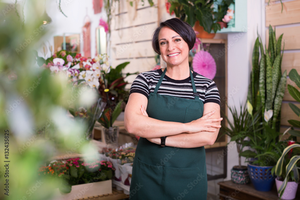 Glad woman florist smiling among the potted plants