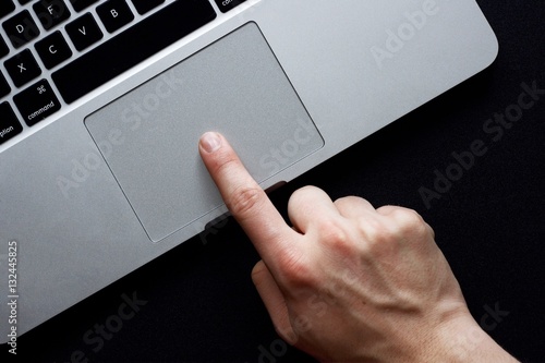 Hand using trackpad on laptop over black background photo