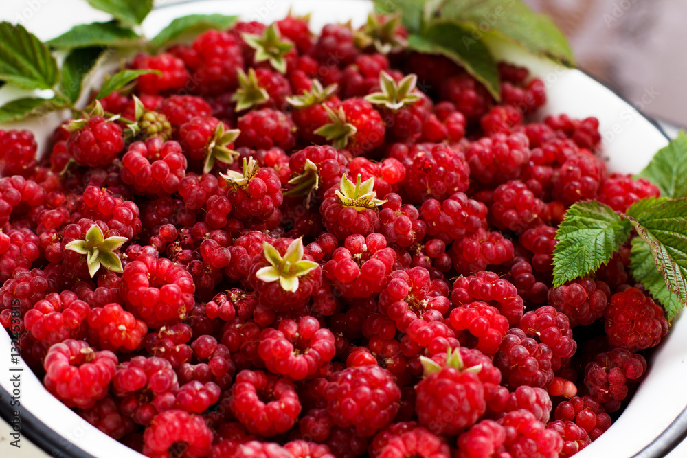 Juicy flavour organic maroon raspberry with grean leaves in white bowl Juicy flavour organic maroon raspberry with grean leaves in white bowl