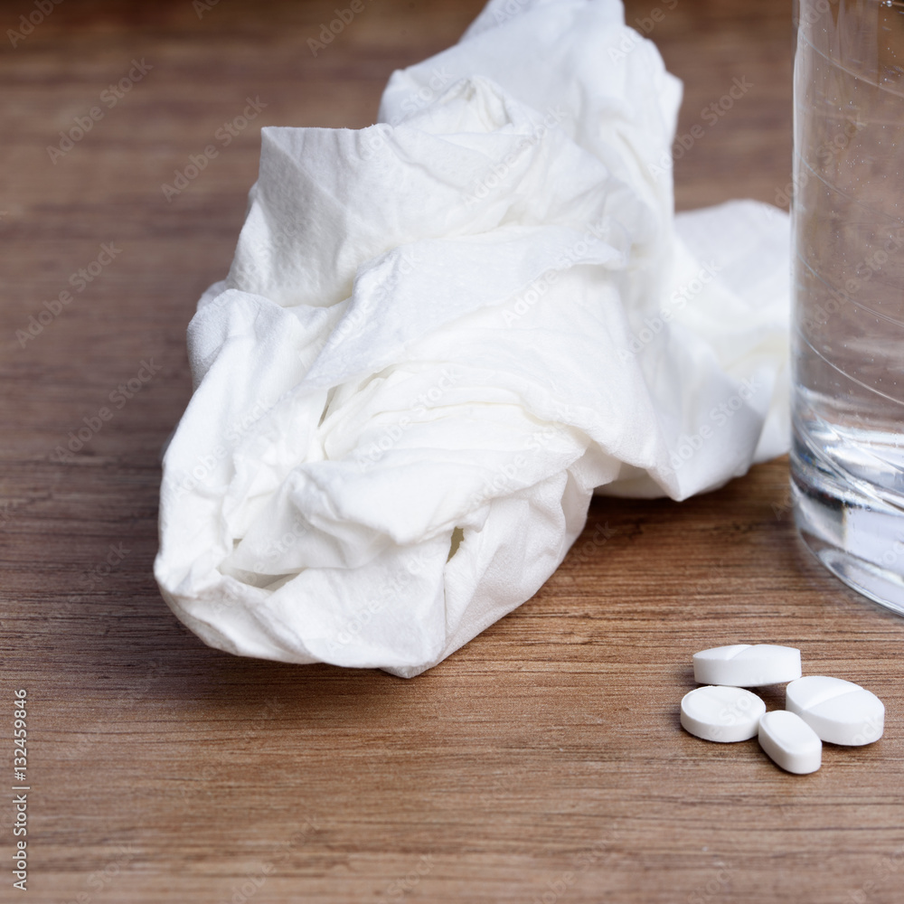 Tabletten neben Papiertaschentuch und einem Glas Wasser Tabletten neben Papiertaschentuch und einem Glas Wasser