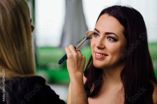 Make-up artist hand applying bright base color on model s face and holding a brush   close .
