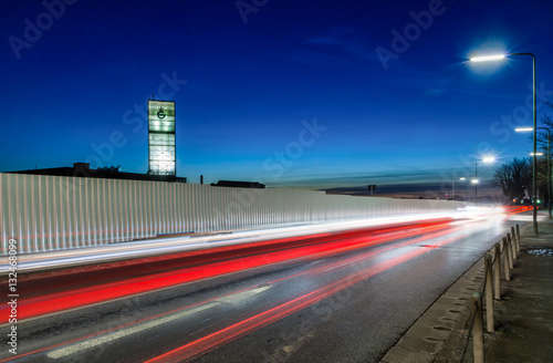 Historical floating glass tower in Dusseldorf during sunset. Light trails in the front. White arrow shows direction.