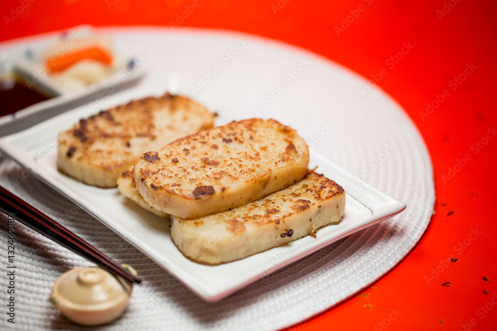 Turnip cake with sauce and white placemat on red background. People will eat turnip cake during Chinese New Year to pray for good fortune.It means be promoted step by step.The Chinese text is 