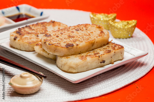 Turnip cake with sauce and white placemat on red background. People will eat turnip cake during Chinese New Year to pray for good fortune.It means be promoted step by step.The Chinese text is "spring"