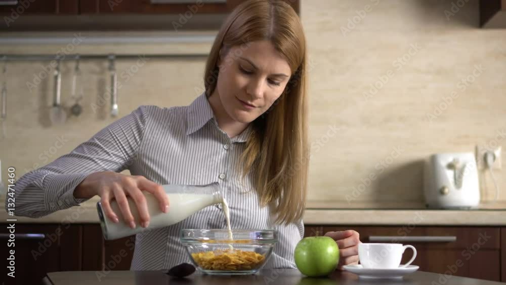 Beautiful young attractive businesswoman pouring milk into a bowl of cornflakes in the kitchen. Beautiful young attractive businesswoman pouring milk into a bowl of cornflakes in the kitchen.