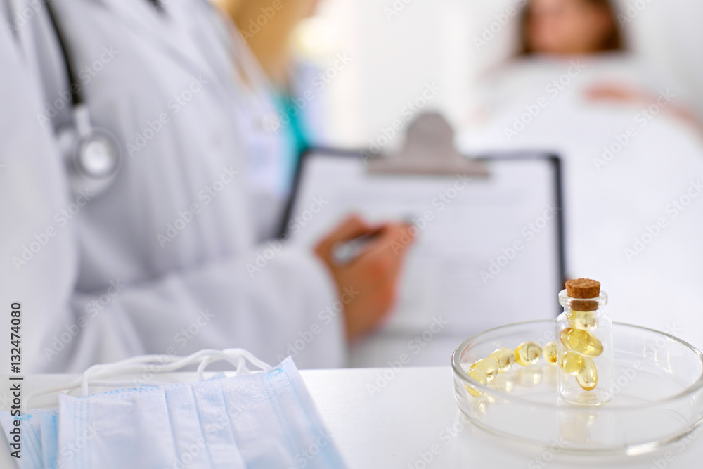 Medicine capsules and pills are lying against the background of a doctor writing prescription. Patient is in the bed and ready to take medication. Medicine capsules and pills are lying against the background of a doctor writing prescription. Patient is in the bed and ready to take medication.