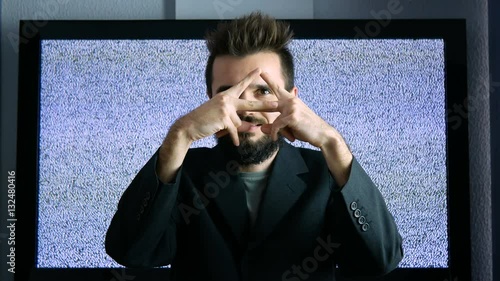 Bearded man in suit showing his eye in triangle as the Eye of Providence while moving forward and backwards with large grainy screen behind him. photo