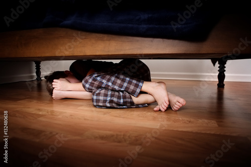 Fearful boy hiding under the bed