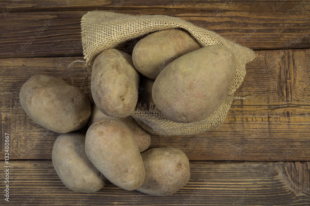 Potatoes from bag lying on wooden background Potatoes from bag lying on wooden background