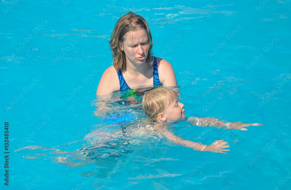 Eine junge Mutter gibt Ihrem Kind den ersten Schwimmunterricht im blauen Wasser