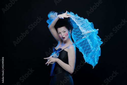 emotional actress brunette woman in an ancient medieval attire and lush hair with white feathers with a white lace umbrella in hand on a black background in the studio