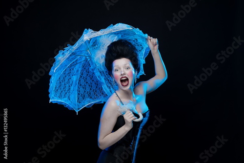 emotional actress brunette woman in an ancient medieval attire and lush hair with white feathers with a white lace umbrella in hand on a black background in the studio