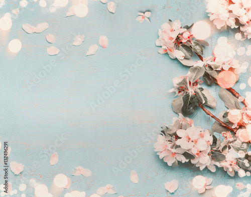 Pretty spring blossom on light blue background with bokeh, top view, pastel color, border