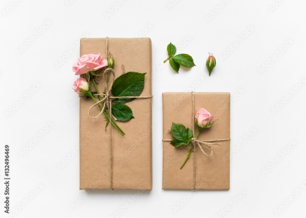 Gift boxes in eco paper on white background. Presents decorated with roses. Holiday concept, top view, flat lay Gift boxes in eco paper on white background. Presents decorated with roses. Holiday concept, top view, flat lay