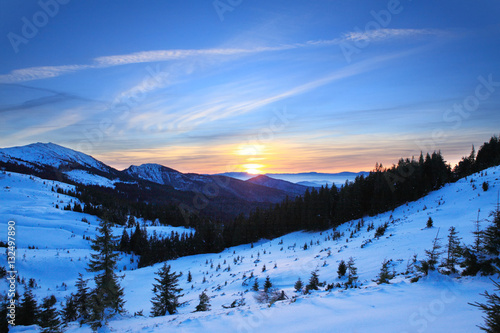 Sunset in winter Carpathians. The setting sun, painted in warm colors covered with snow slopes.