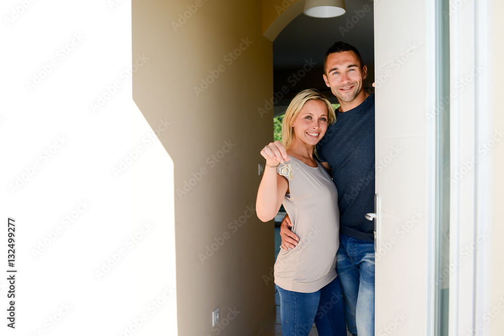 happy young couple at the front door of new house showing proudly home key happy young couple at the front door of new house showing proudly home key