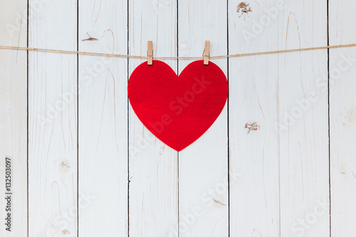 Red heart hanging at clothesline on wood white background with s