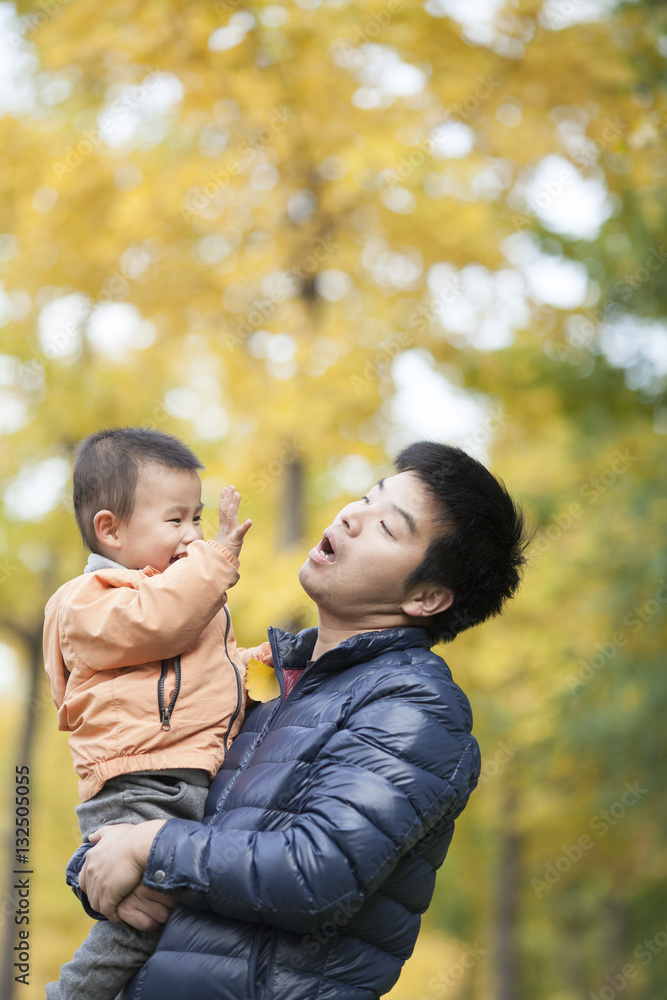 Happy real father and son playing in front of ginkgo trees Happy real father and son playing in front of ginkgo trees