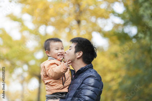 Happy real father and son kissing in front of ginkgo trees