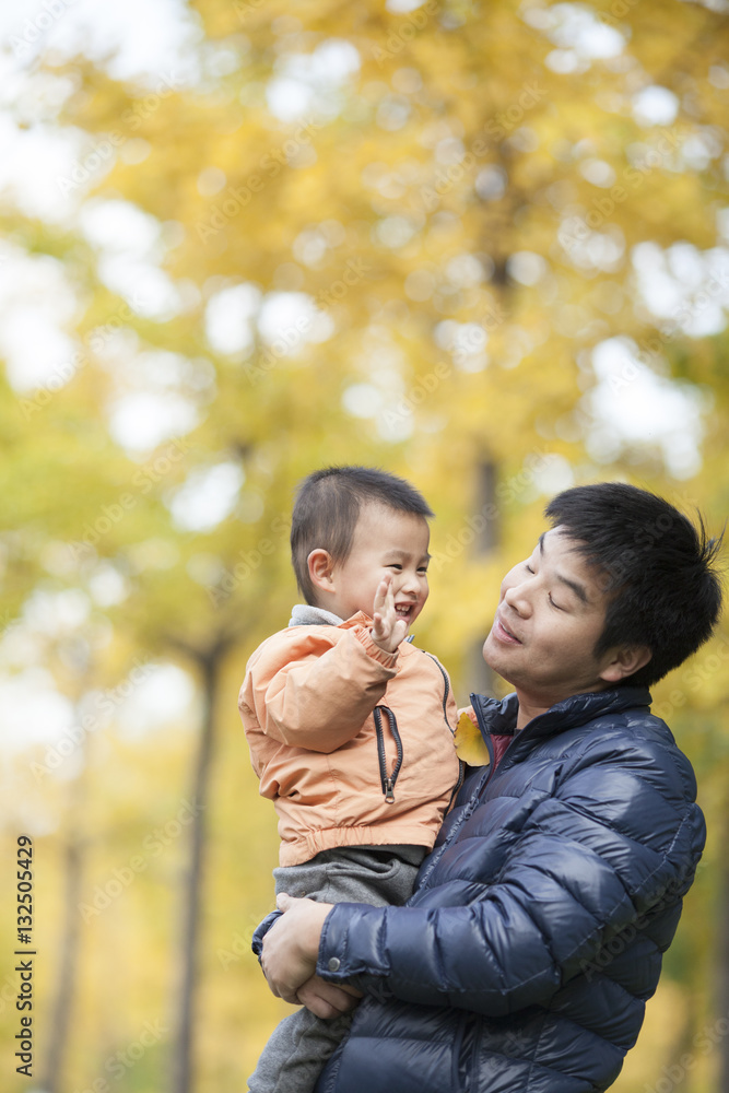 Happy real father and son playing in front of ginkgo trees Happy real father and son playing in front of ginkgo trees