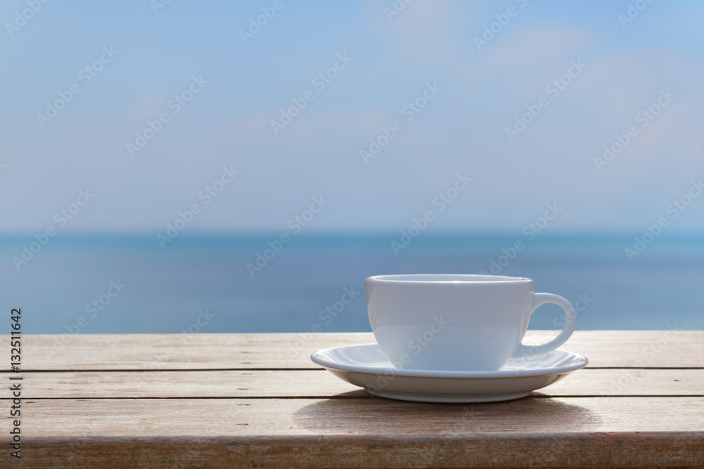 White coffe cup on wood table top with blurred sea sky backgroun