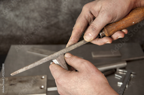 The man saws a piece of stainless steel with file