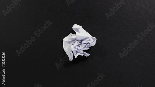 White sheet of paper appears on black background then is quickly crumped and disappears, folded paper. Stop motion. Close up, 4K Ultra HD.