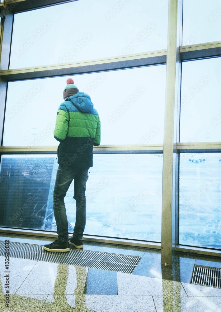 Unrecognizable person standing at a big window in an airport terminal Unrecognizable person standing at a big window in an airport terminal