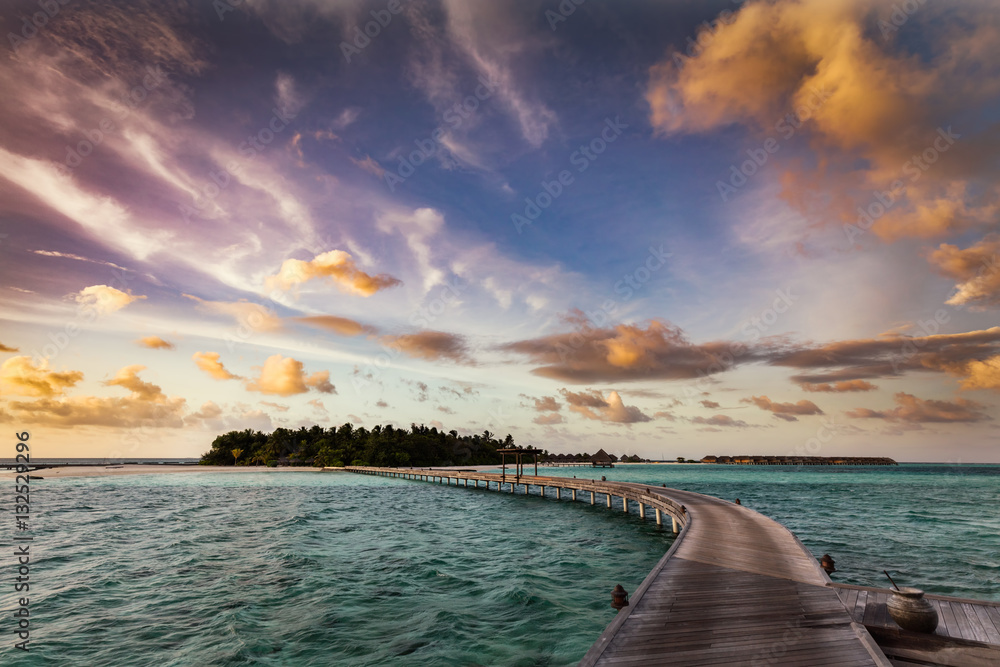Fototapeta premium Wooden jetty towards a small island in Maldives at sunset