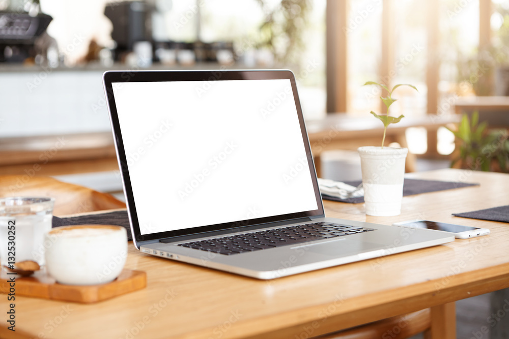 Close up minimalist shot of generic laptop computer and working accessories resting on wooden table against blurred background of cafeteria. Workplace of unknown freelancer. Selective focus Close up minimalist shot of generic laptop computer and working accessories resting on wooden table against blurred background of cafeteria. Workplace of unknown freelancer. Selective focus