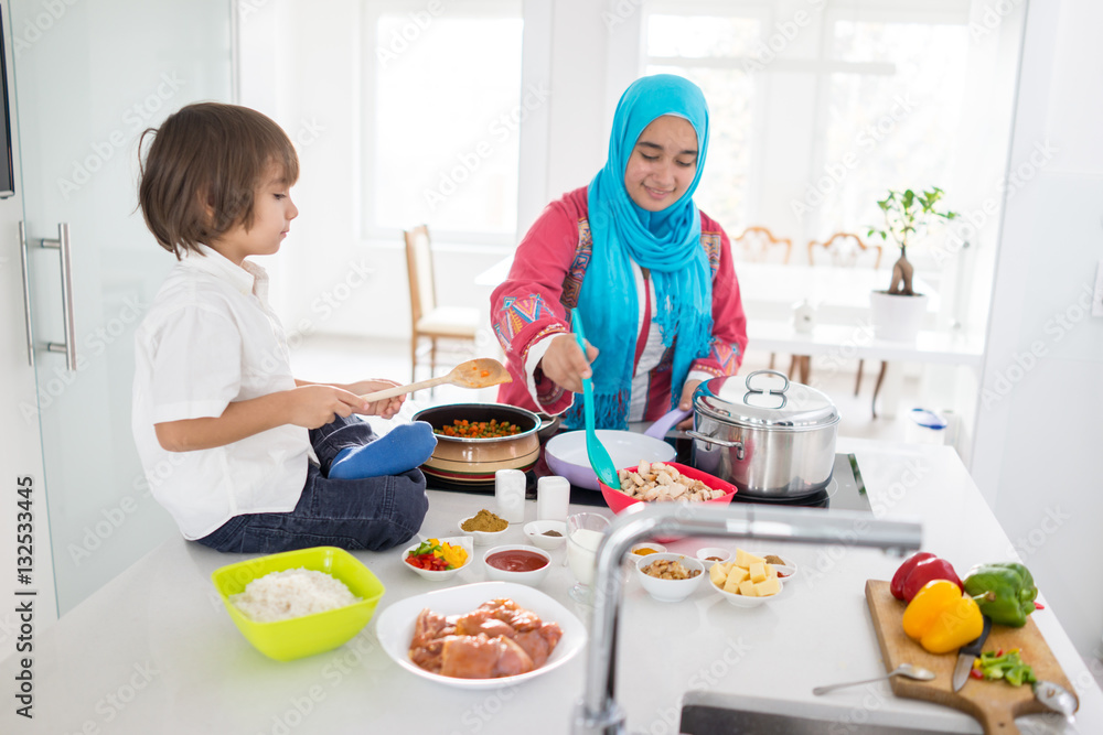 Muslim traditional woman with little son in modern white kitchen Muslim traditional woman with little son in modern white kitchen