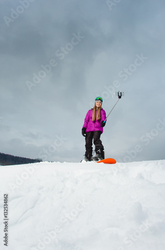 Young woman with the snowboard shooting a selfie by her cell phone 