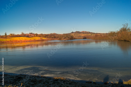 expanse of green grass on the lake with blue sky, countryside and farm around the lake, sunlit water