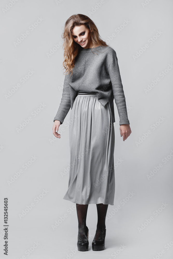 Studio portrait of a full-length stylish young girl in a gray skirt and a gray sweater on a gray background Studio portrait of a full-length stylish young girl in a gray skirt and a gray sweater on a gray background