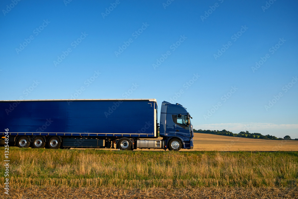 Blue truck traveling on a highway horizon along farm fields of stubble under a blue sky