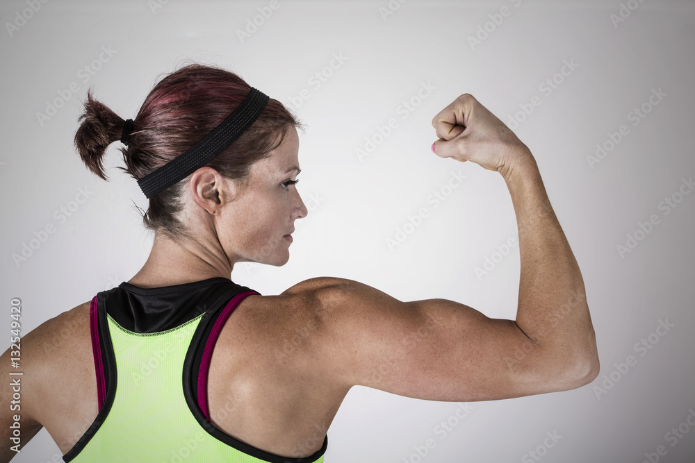Beautiful strong muscular woman flexing her biceps and arm muscles. View  from behind to show her ripped back and arms. Female Body builder Stock  Photo