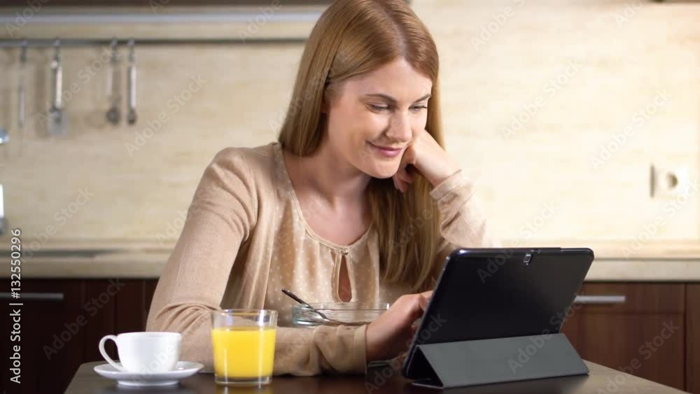 Beautiful young attractive woman having cornflakes for breakfast and using her tablet. Cup of coffee Beautiful young attractive woman having cornflakes for breakfast and using her tablet. Cup of coffee