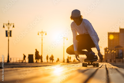 Silhouette of young boy riding longboard on the boardwalk, warm summer time sunset photo