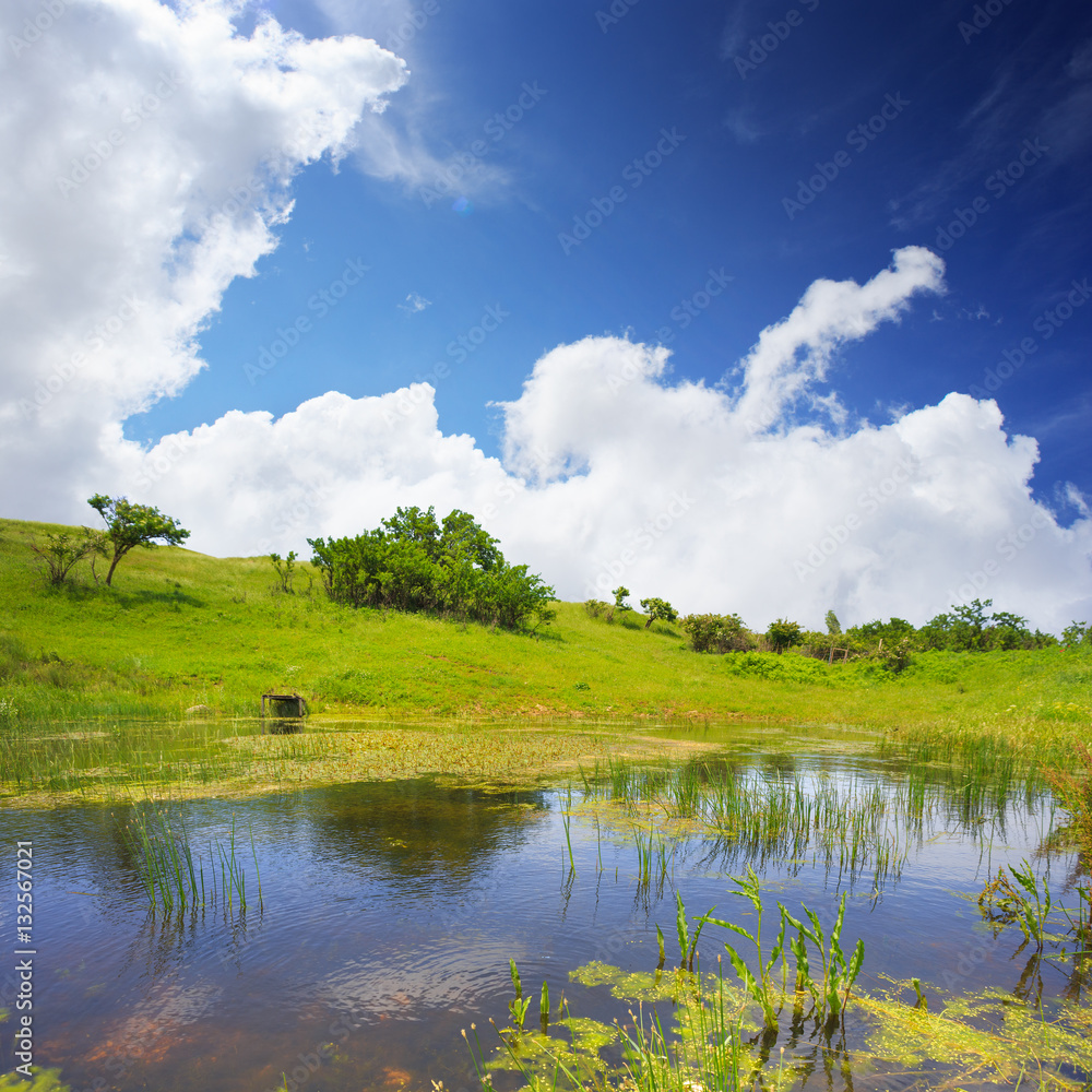 Scenic lake with green spring hills along the shore and blue clo Scenic lake with green spring hills along the shore and blue clo